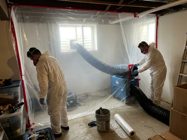 Negative air machine and HEPA air scrubber behind plastic containment with two technicians